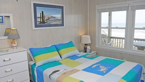 A bedroom with a bed, a dresser, a nightstand, a window with a view, and a framed picture on the wall. - Our Heels in the Sand, a spacious 4-bedroom oceanfront home (Surf City)