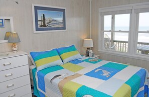 Ein Schlafzimmer mit Bett, Schminktisch, Nachttisch, einem Fenster mit Blick und einem gerahmten Bild an der Wand.