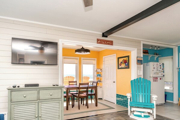 A kitchen with a dining area, a teal Adirondack chair, and a white refrigerator. - Rhyne-O - Cozy & Comfortable Beach Cottage!!! (Surf City)