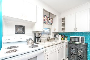 Una cocina moderna con armarios blancos, una estufa blanca, una cafetera y un microondas.