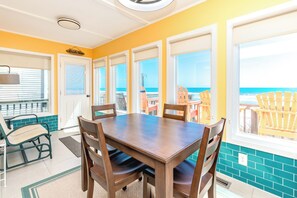 A dining area with a table and chairs, large windows with ocean views, and a balcony with chairs.