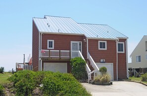 Un edificio di due piani con tetto in metallo, un garage e un piccolo balcone con ringhiera bianca.