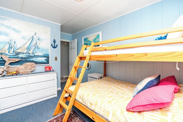 A bunk bed with a ladder, a dresser, a painting of a ship, and a door.
