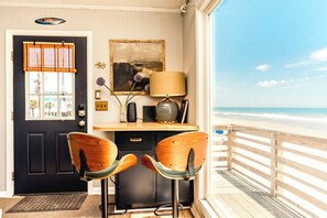 A room with a desk, two chairs, a lamp, a framed picture, and a view of the beach.