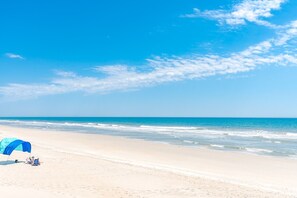 Une plage avec un ciel dégagé, une tente et une mer calme.