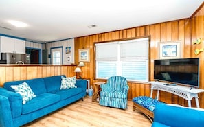 A living room with a blue sofa, a striped armchair, a television, and a small table. - Sea View - 3 bedroom, 2 bath cottage in Surf City!  Dog Friendly! (Surf City)