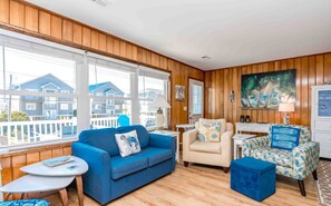 Una sala de estar con un sofá azul, un sillón color beige y otro sillón estampado. Hay una mesita redonda con una lámpara, y un cuadro en la pared.