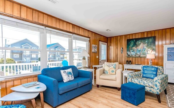 A living room with a blue sofa, a beige armchair, and a patterned armchair. There is a small round table with a lamp, and a painting on the wall. - Sea View - 3 bedroom, 2 bath cottage in Surf City! Dog Friendly! (Surf City)