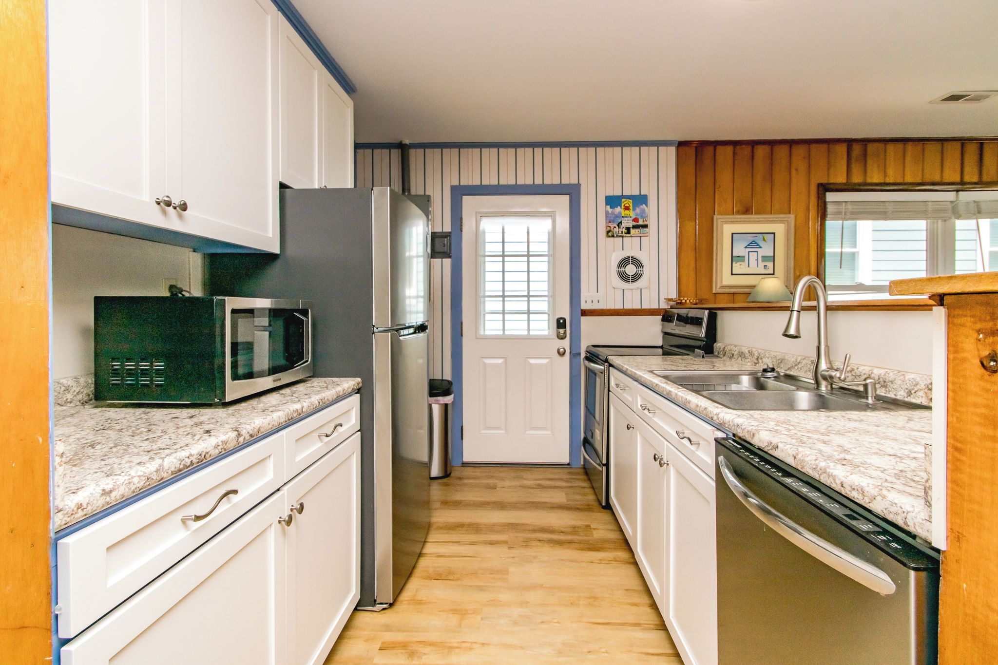 Una cocina con armarios blancos, microondas, refrigerador, lavaplatos y fregadero.