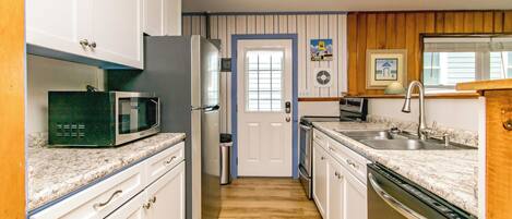 Una cocina con armarios blancos, microondas, refrigerador, lavaplatos y fregadero.