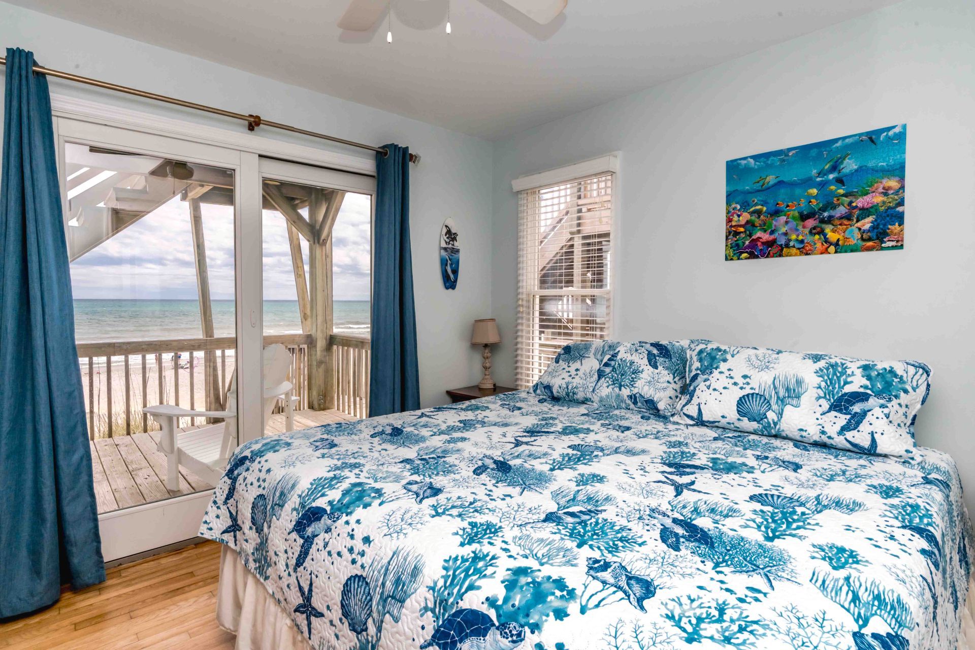 Un dormitorio con cama, vista a la playa, un cuadro y una ventana con cortinas.
