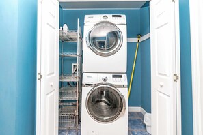 A laundry room with two stacked front-loading washing machines, a metal drying rack, and a yellow measuring tape.