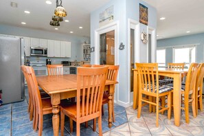 A kitchen with white cabinets, a microwave, and a dining area with wooden chairs and a table. - Simple Pleasure Oceanfront in Surf City, NC—perfect for 15! (Surf City)