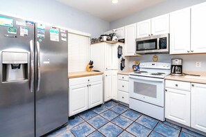 A kitchen with white cabinets, a stainless steel refrigerator, a microwave, and a stove.
