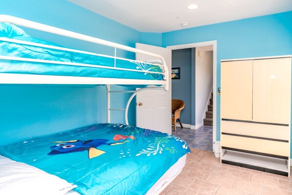 A room with a bunk bed, a wardrobe, and a door leading to another room.