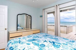 A bedroom with a bed, a dresser, a mirror, and a view of the beach through a sliding glass door. - Simple Pleasure Oceanfront in Surf City, NC—perfect for 15! (Surf City)