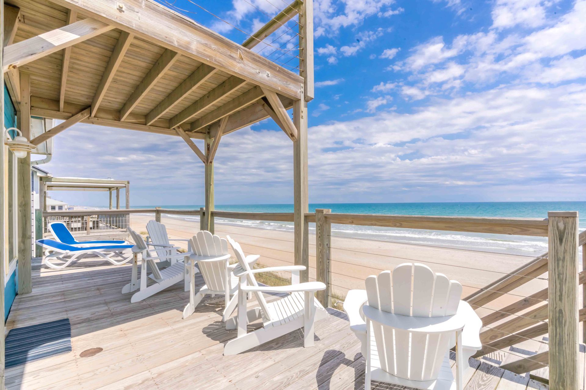 A wooden deck with beach chairs and a pool area overlooking the ocean.