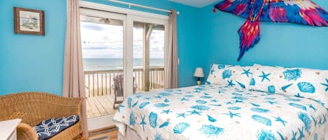 A bedroom with a bed, a wicker chair, a view of the ocean, and a colorful bird decoration.