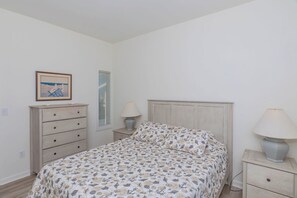 A bedroom with a bed, a dresser, a nightstand, a lamp, a window with blinds, and a framed picture on the wall.