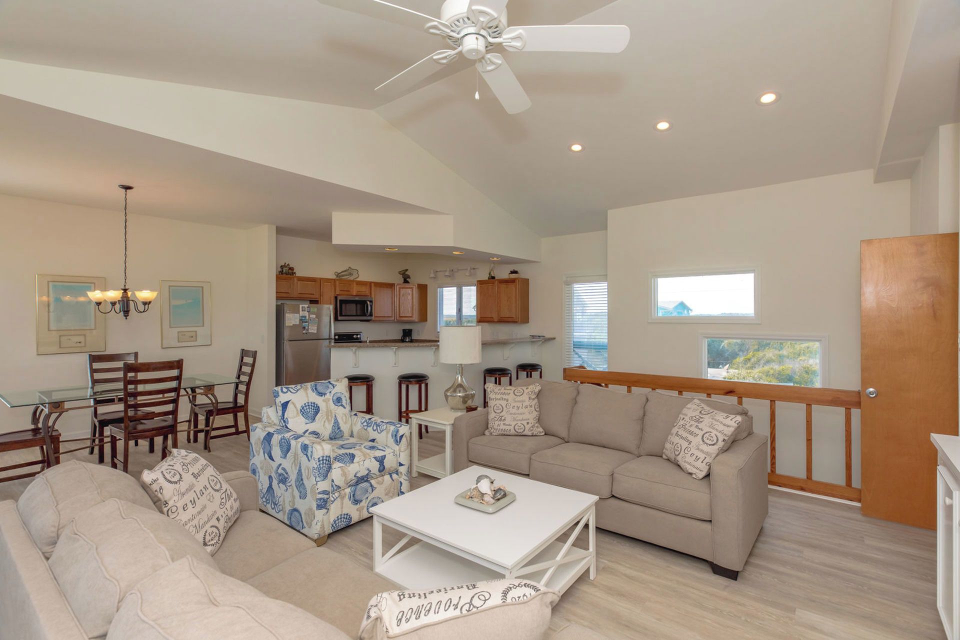 A spacious living room with a ceiling fan, a dining area with a glass table, and a kitchen with wooden cabinets.
