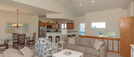 A spacious living room with a ceiling fan, a dining area with a glass table, and a kitchen with wooden cabinets.