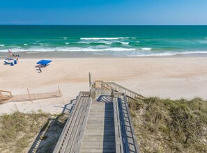 A wooden boardwalk leading to a sandy beach with a clear view of the ocean.