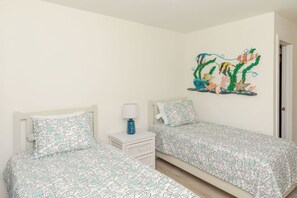 A bedroom with two single beds, a nightstand with a lamp, and a wall mural of fish and coral.
