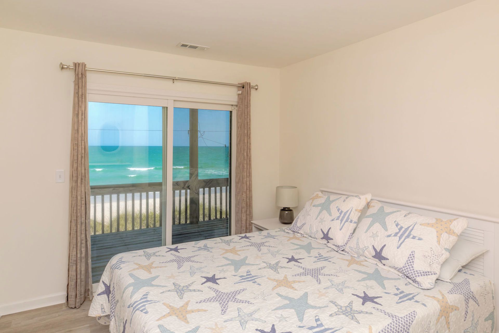 A bedroom with a bed, a nightstand, a lamp, and a view of the ocean through a sliding door.