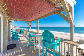 A wooden deck with turquoise chairs and a red canopy overlooking a beach.
