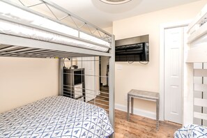 A bunk bed room with a TV mounted on the wall, a small table, and a door.