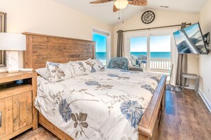 A bedroom with a wooden headboard, a bed with floral bedding, a television, and a view of the ocean. - Surf Club - Oceanfront, 3 bedroom, gorgeous home in Surf City!  Dog Friendly! (Surf City)