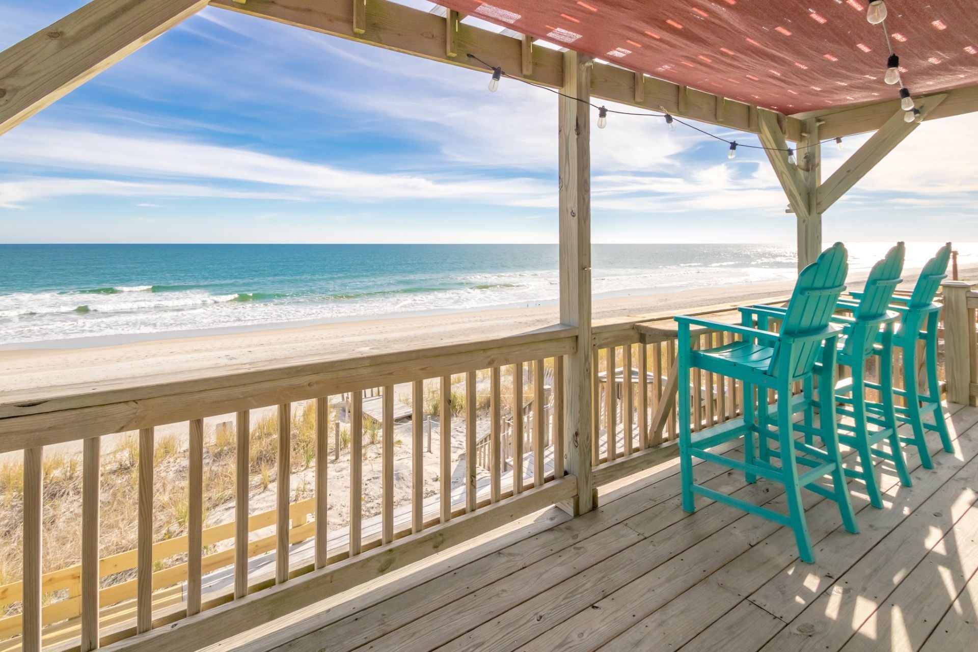A wooden deck with a view of the ocean, featuring a covered area with chairs.