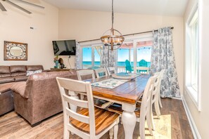 A dining area with a wooden table, white chairs, and a view of the sea.