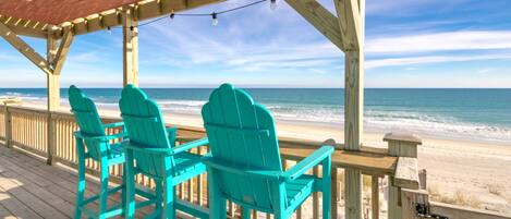 A wooden deck with turquoise Adirondack chairs facing the beach.