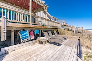 Um deck de madeira com cadeiras de praia e uma mesa, com vista para a praia.