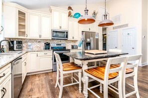 A kitchen with white cabinets, a stainless steel refrigerator, a microwave, and a wooden dining table with chairs. - Surf Club - Oceanfront, 3 bedroom, gorgeous home in Surf City!  Dog Friendly! (Surf City)