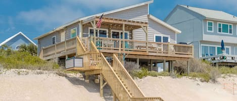 A beachfront property with a wooden staircase leading to a deck, a flag, and a clear sky.