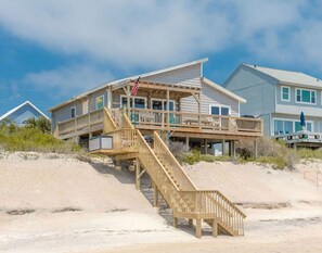 A beachfront property with a wooden staircase leading to a deck, a flag, and a clear sky. - Surf Club - Oceanfront, 3 bedroom, gorgeous home in Surf City!  Dog Friendly! (Surf City)