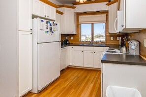 Una cocina con armarios blancos, un refrigerador, una estufa y un ventanal.