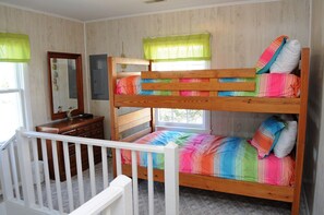 Una cama individual superpuesta con ropa de cama colorida, un aparador con espejo y una ventana con cortinas.