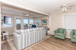 A living room with a striped sofa, two green armchairs, a ceiling fan, and a view of the outdoors through large windows. - Tumble Inn - Oceanfront home in Topsail Beach! Gazebo & Dog Friendly! (Topsail Beach)
