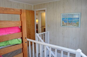 A room with a bunk bed, a white railing, and a beach-themed painting on the wall.