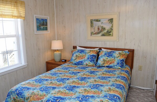 A bedroom with a bed, a nightstand, a lamp, and two framed pictures on the wall. - Tumble Inn - Oceanfront home in Topsail Beach! Gazebo & Dog Friendly! (Topsail Beach)