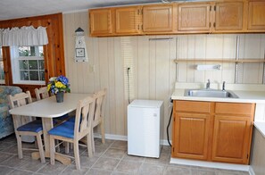 A compact kitchen with wooden cabinets, a white refrigerator, a sink, and a dining area with a table and chairs. - Tumble Inn - Oceanfront home in Topsail Beach! Gazebo & Dog Friendly! (Topsail Beach)
