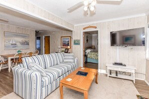 A living room with a striped sofa, a wooden coffee table, a television, and a dining area with chairs and a table. - Tumble Inn - Oceanfront home in Topsail Beach! Gazebo & Dog Friendly! (Topsail Beach)