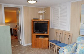 Un espacio habitable compacto con una televisión sobre un mueble de madera, una silla pequeña y un armario de madera.