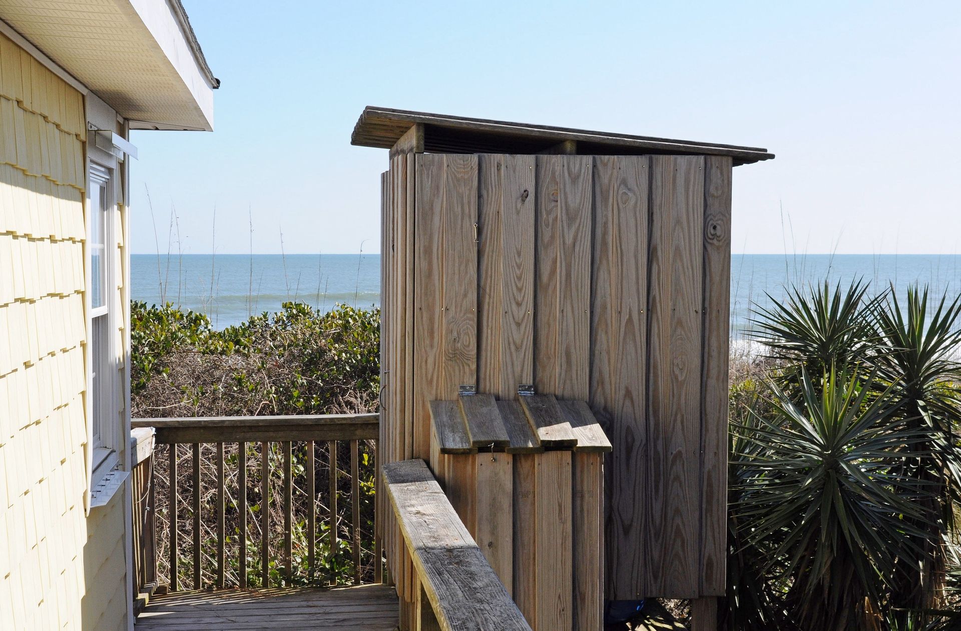 A wooden structure with a sloped roof, possibly a deck or a small building, adjacent to a building with a balcony overlooking a body of water.
