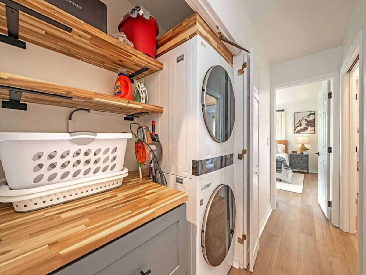 A laundry room with two front-loading washing machines, wooden shelves with laundry baskets, and a red bucket.