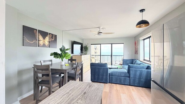 A modern living room with a dining area, a ceiling fan, and a large window overlooking the sea. - OD tower II #12, ocean view Fantastic condo + pool (Myrtle Beach)