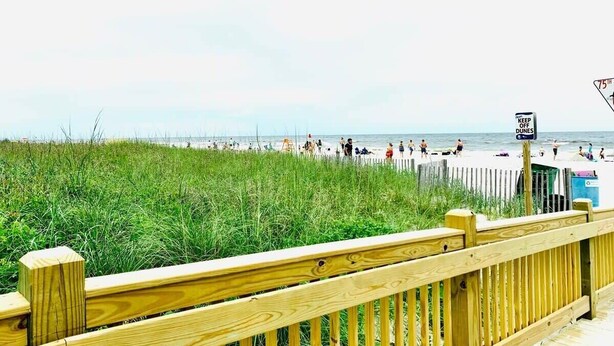 A beach with a wooden boardwalk, a sign that says "KEEP OFF DUNES," and people enjoying the beach. - Ocean Dunes Villas #22, stay close to the ocean (Myrtle Beach)